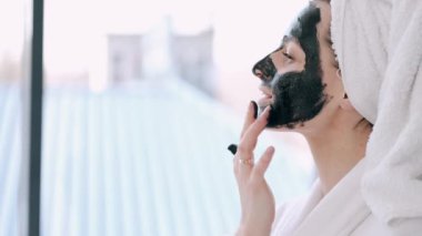 Havluya sarılı saçları olan güzel bir kadın yüzüne siyah maske takıyor.