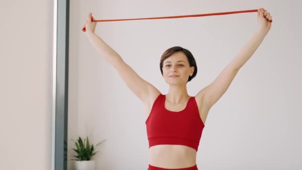 Sportovní žena v červeném kostýmu cvičení s fitness kapelou — Stock video
