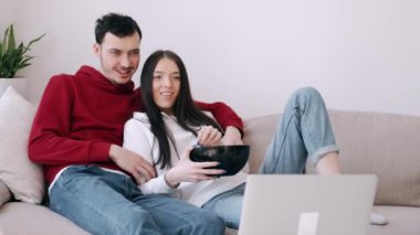 Güzel genç çift dizüstü bilgisayarda film izliyor ve patlamış mısır yiyor.
