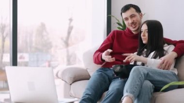 Güzel genç çift dizüstü bilgisayarda film izliyor ve patlamış mısır yiyor.