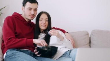Güzel genç çift dizüstü bilgisayarda film izliyor ve patlamış mısır yiyor.