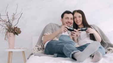 Güzel kız ve erkek arkadaş yatakta playstation oynuyorlar.