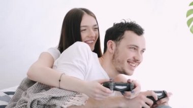 Güzel kız ve erkek arkadaş yatakta playstation oynuyorlar.