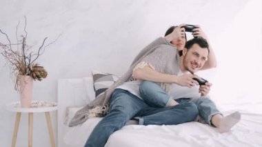 Güzel kız ve erkek arkadaş yatakta playstation oynuyorlar.