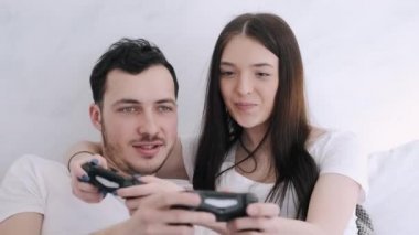 Güzel kız ve erkek arkadaş yatakta playstation oynuyorlar.