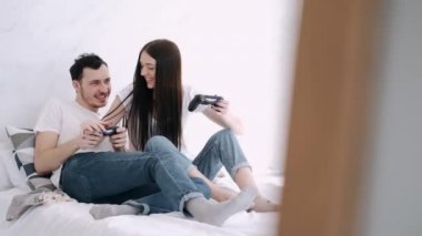 Güzel kız ve erkek arkadaş yatakta playstation oynuyorlar.
