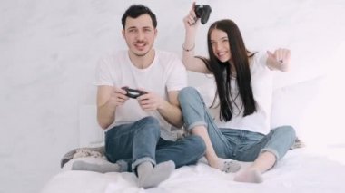Güzel kız ve erkek arkadaş yatakta playstation oynuyorlar.
