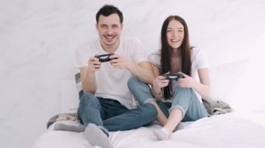 Güzel kız ve erkek arkadaş yatakta playstation oynuyorlar.