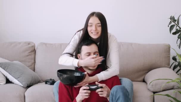 Joven niño está jugando videojuegos y la chica está alimentando a su novio en una habitación — Vídeos de Stock