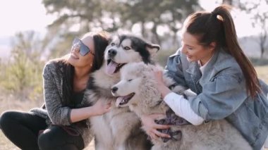 Genç güzel kadınlar gülümsüyor ve sevimli köpekleriyle sarılıyorlar.