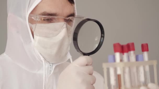 Científico masculino está examinando los análisis de sangre con una lupa — Vídeo de stock