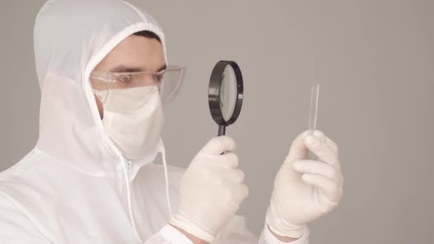 덮개 장비를 갖춘 남성 연구원 이 실험실에서 현미경 유리를 검사하고 있습니다. — 비디오