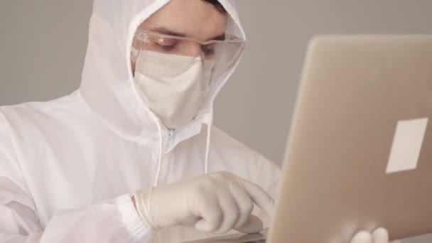 Man scientist in a full-covering equipment is doing research on laptop — Stock Video