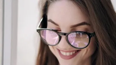 Gözlüklü güzel kadın pencerenin yanında gülümsüyor.