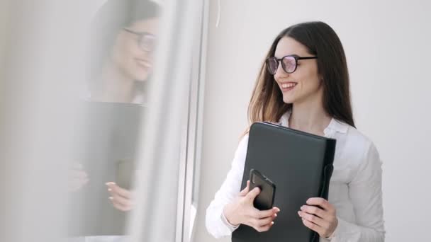 Hermosa mujer en gafas está cerca de la ventana sonriendo — Vídeo de stock