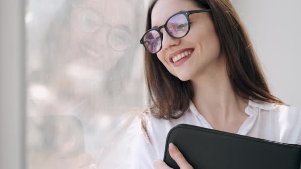 Hermosa mujer en gafas está cerca de la ventana sonriendo — Vídeo de stock