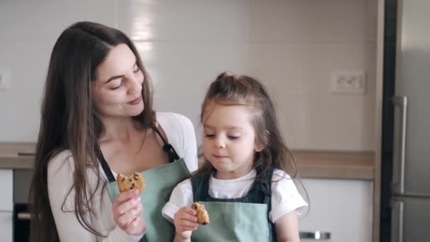 Vacker mor och dotter äter kakor i ett kök. — Stockvideo