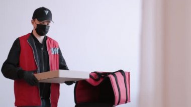 Koruyucu ekipmanlı teslimatçı paket pizza getiriyor.