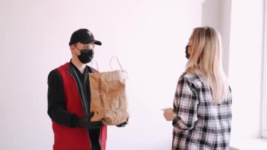 Teslimatçı, maske takan bir kadına kağıt torba veriyor.