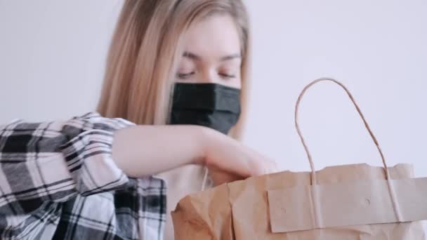 Donna in una maschera protettiva nera sta disimballando un sacchetto di carta artigianale — Video Stock