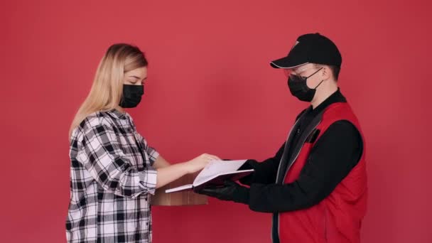 Kvinnan i mask tar emot ett paket från en budbärare och signerar ett dokument. — Stockvideo