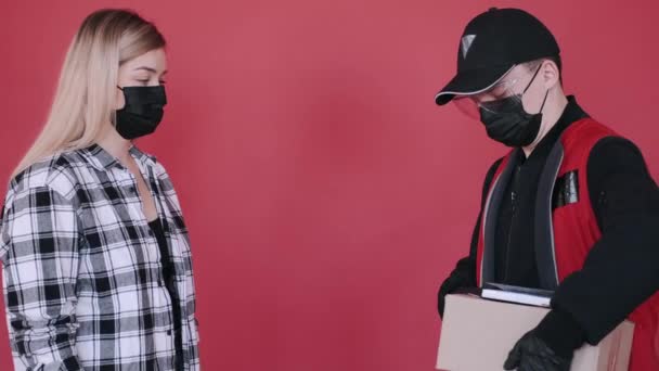 Een vrouw met een masker ontvangt een pakje van een bezorger en tekent een document. — Stockvideo