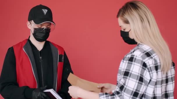 Een vrouw met een masker ontvangt een pakje papieren enveloppen van een bezorger. — Stockvideo