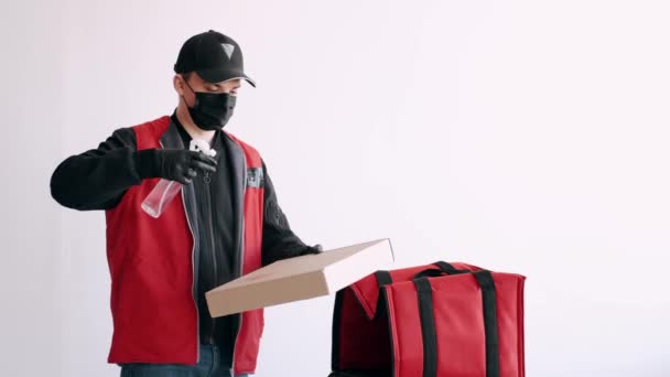 Deliveryman in una maschera e guanti sta spruzzando antisettico su una scatola di pizza — Video Stock