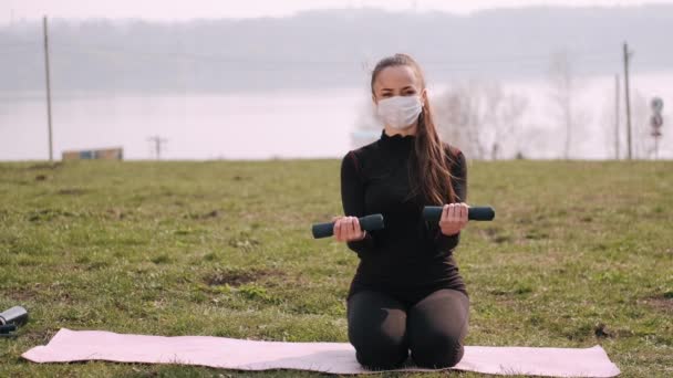 Atletische vrouw in een beschermend masker doet oefening met halters — Stockvideo