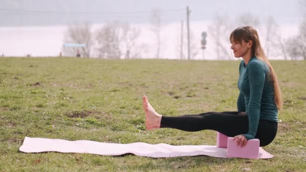 Спортивная женщина делает растяжку на коврике на газоне — стоковое видео