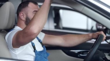 Mavi üniformalı tamirci servis merkezinde arabayı test ediyor.