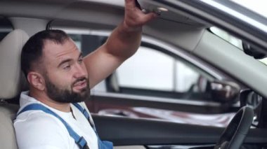 Mavi üniformalı tamirci servis merkezinde arabayı test ediyor.
