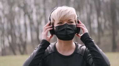 Maskeli atletik kadın kulaklıkla müzik dinliyor.