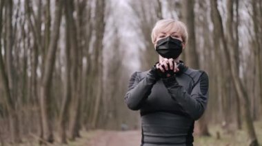 Maskeli orta yaşlı bir kadın dışarıda sabah egzersizi yapıyor.