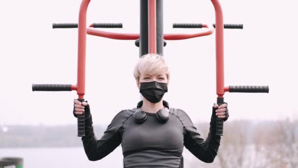 The sporty woman in a protective mask is doing workout in a park — Stock Video