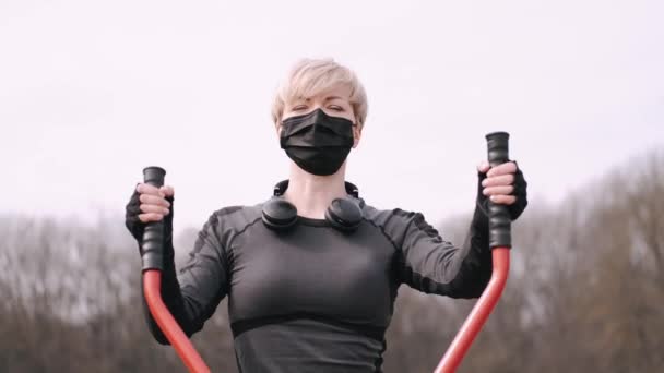 La donna sportiva con una maschera protettiva sta facendo allenamento in un parco — Video Stock