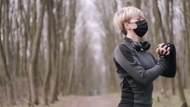 Een vrouw van middelbare leeftijd met een masker doet ochtendtraining buiten. — Stockvideo