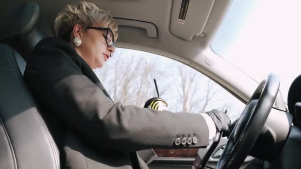 Uma mulher de negócios de óculos está trabalhando e bebendo um café em um carro — Vídeo de Stock