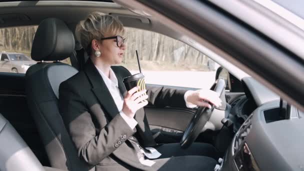 La empresaria de negro está conduciendo un coche y bebiendo un café para llevar — Vídeos de Stock