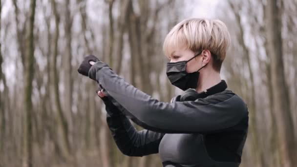Kobieta w średnim wieku w masce wykonuje poranne ćwiczenia na zewnątrz — Wideo stockowe