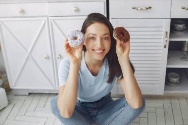 Güzel bir kız mutfakta donutla duruyor.