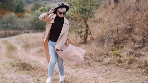 Retrato de mujer con estilo en abrigo y sombrero moviéndose en el bosque — Vídeos de Stock