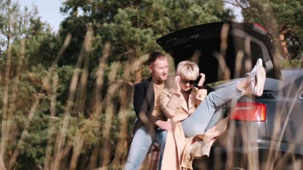 Man en vrouw zitten op de kofferbak en knuffelen in de natuur — Stockvideo