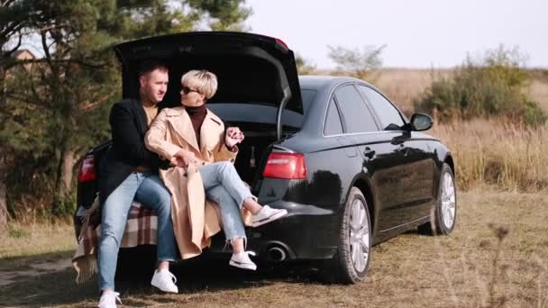 Mąż i żona siedzą na bagażniku samochodu i przytulają się w naturze — Wideo stockowe