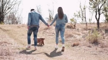 Kot giyen genç adam ve kadın buğday tarlasında bir köpekle yürüyorlar.