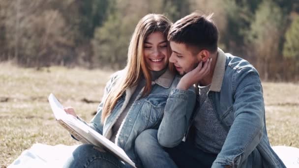 Atractivo joven está abrazando a su novia leyendo un libro en el campo — Vídeo de stock