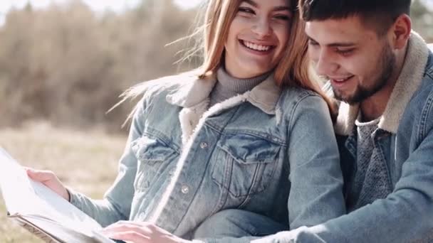 Atractivo joven está abrazando a su novia leyendo un libro en el campo — Vídeo de stock