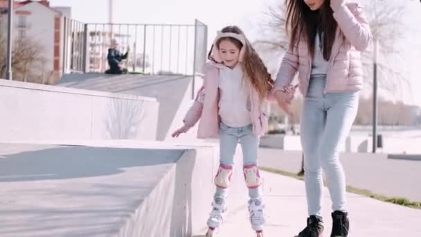 A mulher está a ajudar a criança a andar de patins num parque de skate lá fora. — Vídeo de Stock