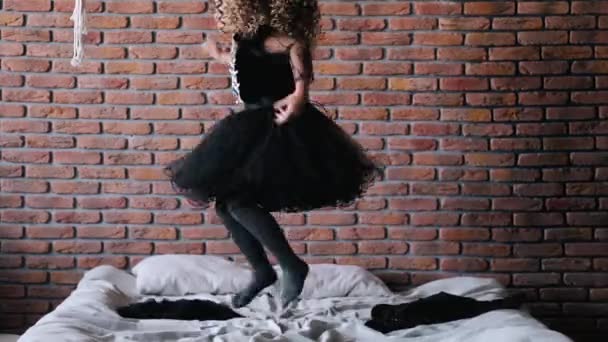 Meisje met krullend haar in zwarte jurk dumpen op bed — Stockvideo