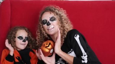 Cadılar Bayramı kostümlü kız ve anne kırmızı kanepede oynuyorlar.